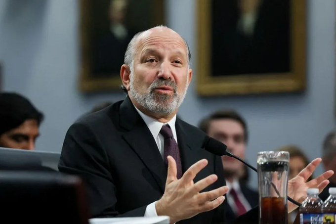A bald man with a gray beard, wearing a dark suit and red tie, speaks emphatically with both hands raised while seated at a hearing room table featuring a microphone and water bottle, with framed portraits visible on the wall behind him. The image does not depict the crypto executives (Brian Armstrong, Chris Dixon, Brad Garlinghouse, and Arjun Sethi) mentioned in the post; the identity of the man shown is not confirmed from the image alone, though the accompanying text suggests it may relate to Commerce Secretary Howard Lutnick ahead of the White House crypto meeting.