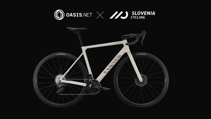 A white Canyon road bike is displayed against a black background, positioned between the "OASIS.NET" and "SLOVENIA CYCLING" logos at the top. The image's cycling theme and partnership branding tie into the post's mention of trivia night and race-reading challenges, suggesting the brand sponsors or relates to competitive cycling content.