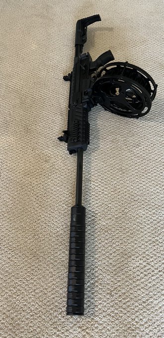 A Fostech Origin 12 tactical shotgun lies on a carpet, fitted with a long suppressor on the extended barrel and a distinctive 30-round drum magazine, ready for high-capacity home defense. The image directly illustrates the post's call for pairing the Origin-12 with a suppressor and drum mag for maximum "FAFO" readiness.