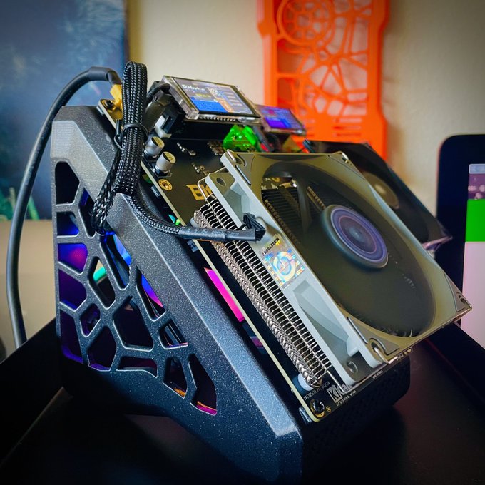 A custom-built computer/mining rig with exposed components including a large cooling fan, graphics card, and circuit board with RGB lighting in a dark case with geometric cutouts.
