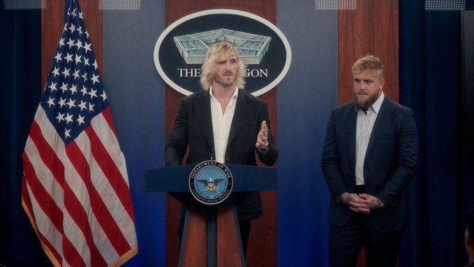 Two men with blonde hair stand at a podium bearing the seal of the President of the United States, positioned in front of an American flag and a Pentagon logo, appearing to be a satirical depiction from a TV show.