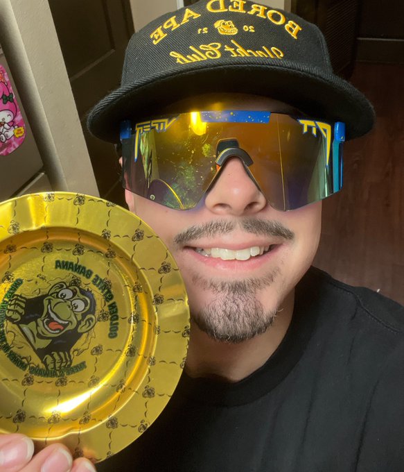 The image features a man wearing sunglasses, a hat with "Bored Ape" written on it, and holding up a gold plate with a cartoon monkey design. The caption reads, "I am a Bored Ape. I am part of the best Club on the internet. I celebrate the community we've built."